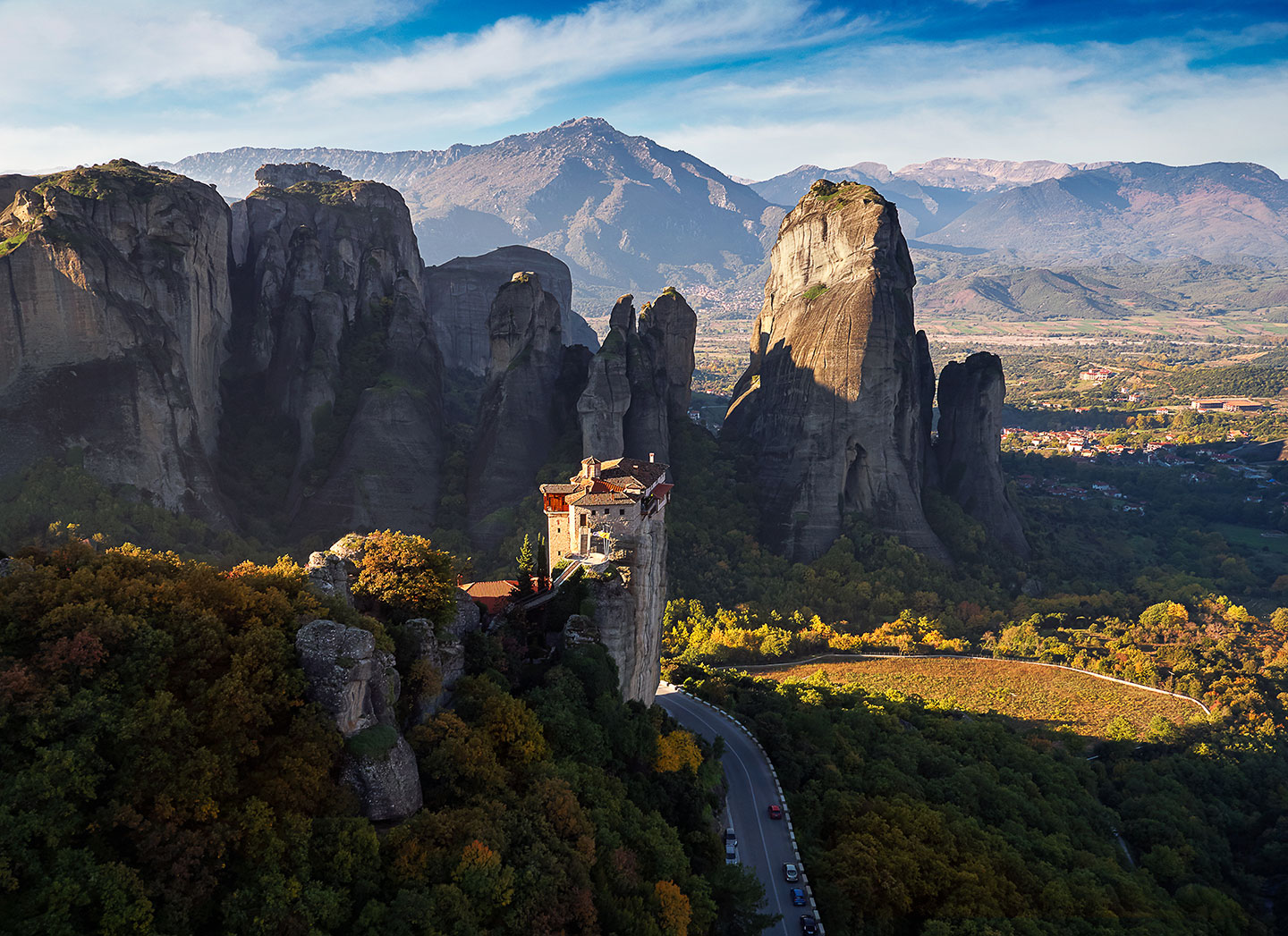 (Morning light streams through the valley and illuminates a lonely monastery in Meteora Greece.)